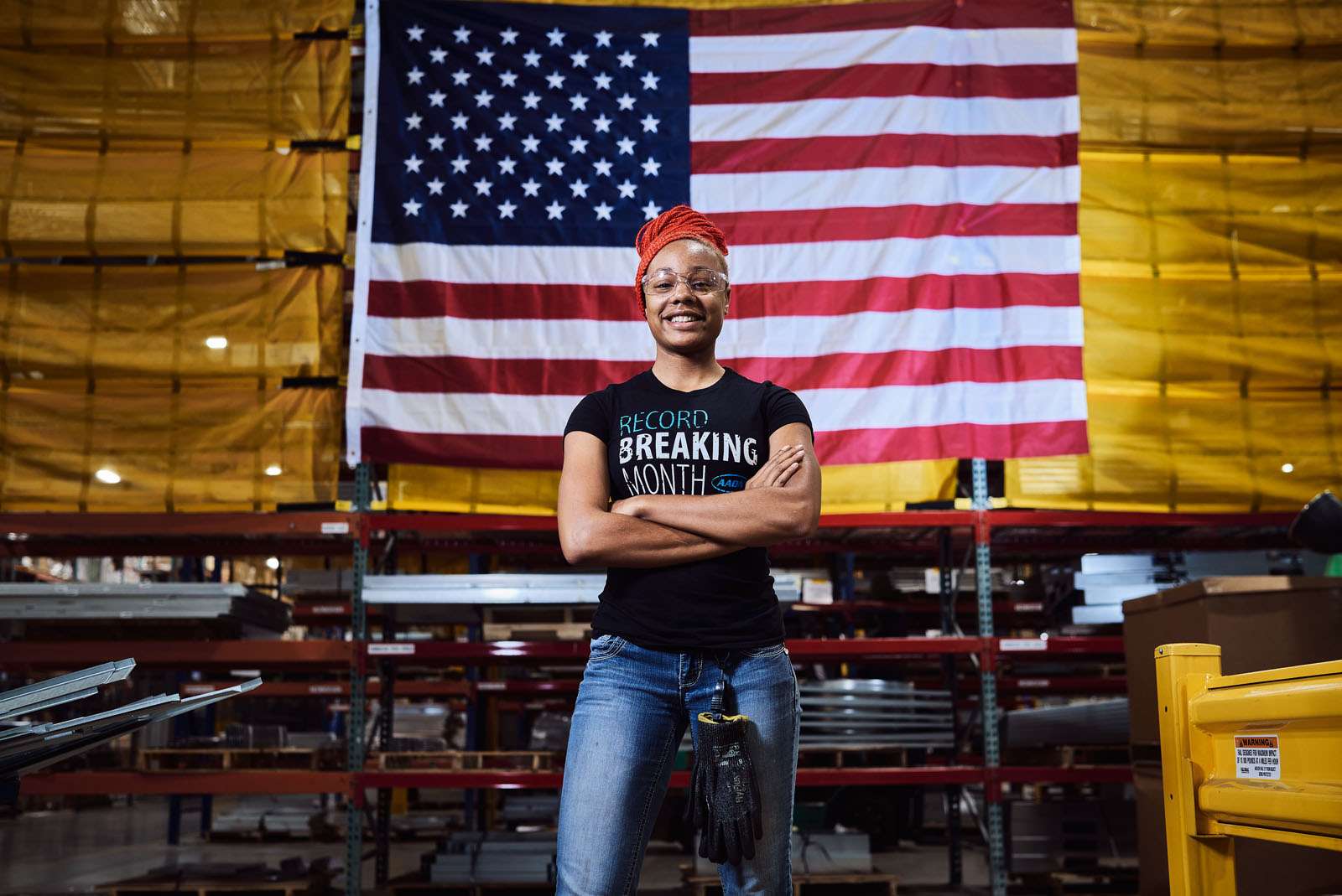 a Woman in an Orange Headwrap and Glasses Stands Confidently by a U.s. Flag in an Industrial Warehouse During a Work Event. Commercial Photography – Amatucci Photography - Amatucci Photography A woman in an orange headwrap and glasses stands confidently by a u S Flag in an industrial warehouse during a work event Commercial photography amatucci photography