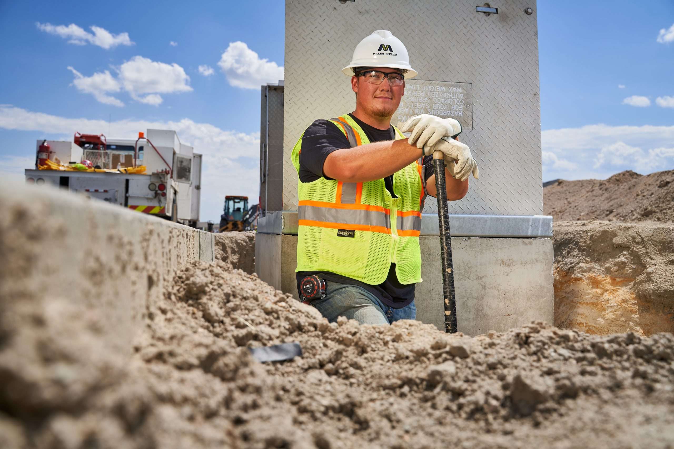 at a Sandy Construction Site in Houston, a Worker in Safety Gear Grips a Metal Rod Near Trucks and Machinery Under Sunny Skies. Commercial Photography – Amatucci Photography - Amatucci Photography At a sandy construction site in houston a worker in safety gear grips a metal rod near trucks and machinery under sunny skies Commercial photography amatucci photography