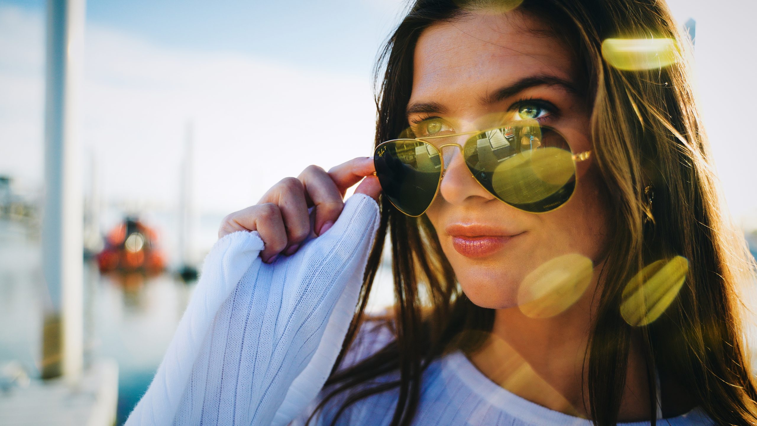 a Woman in Reflective Sunglasses and a White Sweater Adjusts Her Glasses at Deauville Inn, Sunlit Marina and Boats Behind Her. – Amatucci Photography - Amatucci Photography A woman in reflective sunglasses and a white sweater adjusts her glasses at deauville inn sunlit marina and boats behind her amatucci photography