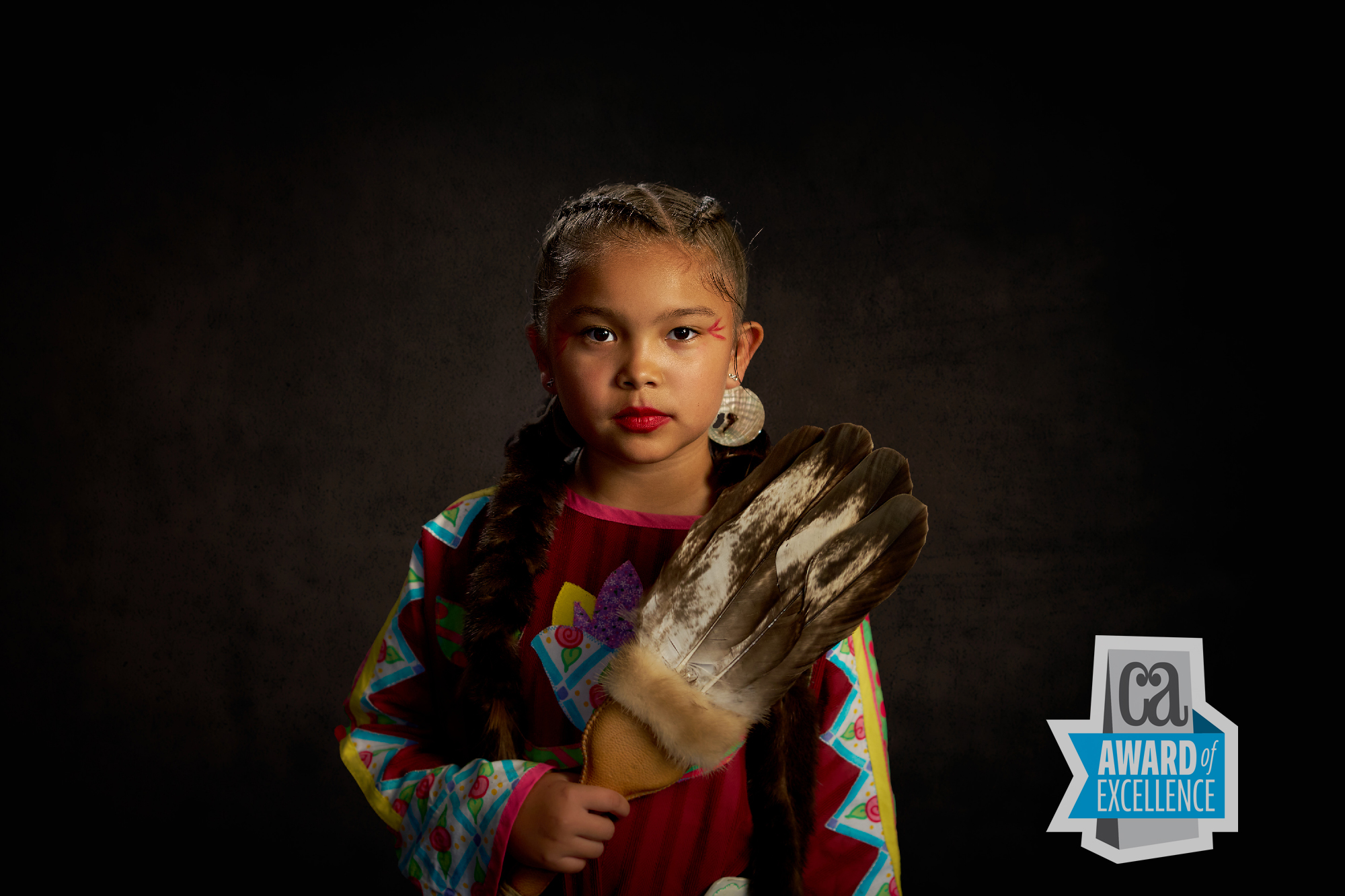 a Calm Young Girl in Vibrant Native Attire Holds Feather Fan at a Puyallup Tribe Portrait Event, Ca Award of Excellence Badge Behind. – Amatucci Photography - Amatucci Photography A calm young girl in vibrant native attire holds feather fan at a puyallup tribe portrait event ca award of excellence badge behind amatucci photography